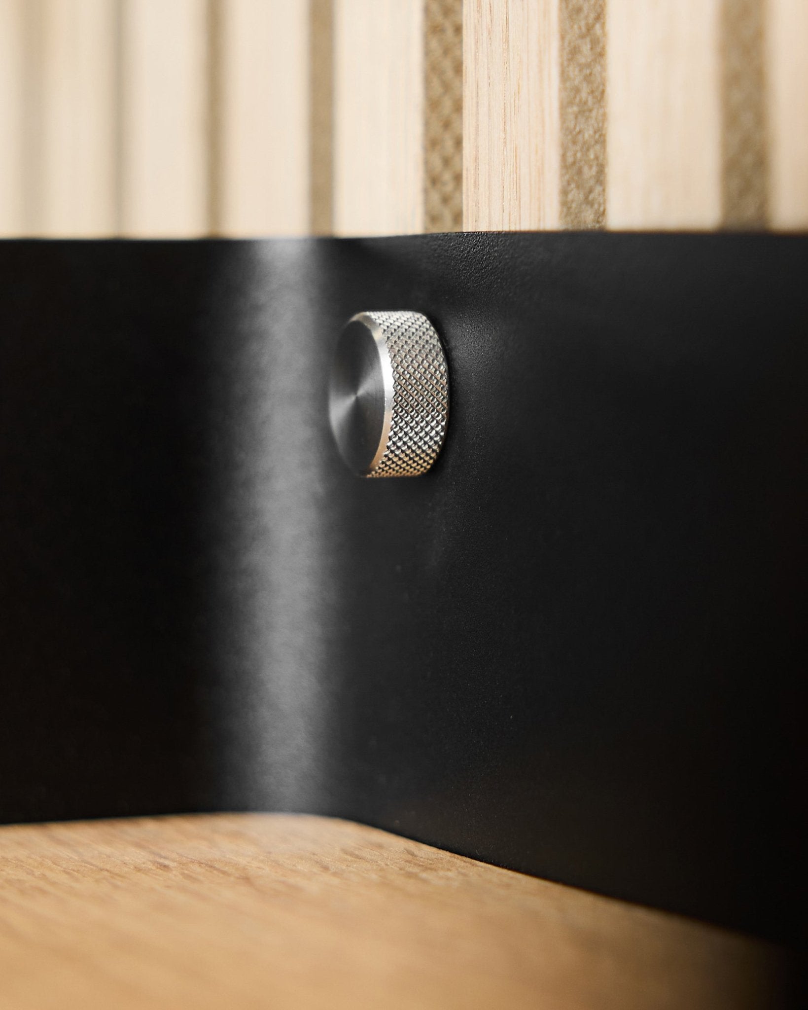 Close-up van twee WoodUpp Finger-schroeven (M5x10 mm, 20x8.8 roestvrij staal steel) op een black metalen oppervlak, met Akupanel akoestische houten latten op de achtergrond.